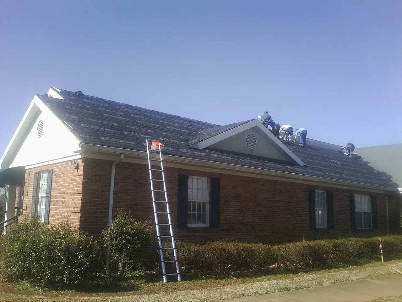 Crew tearing shingles off a brick ranch roof with a ladder set — Emergency Roof Repair work by our crew in Morven