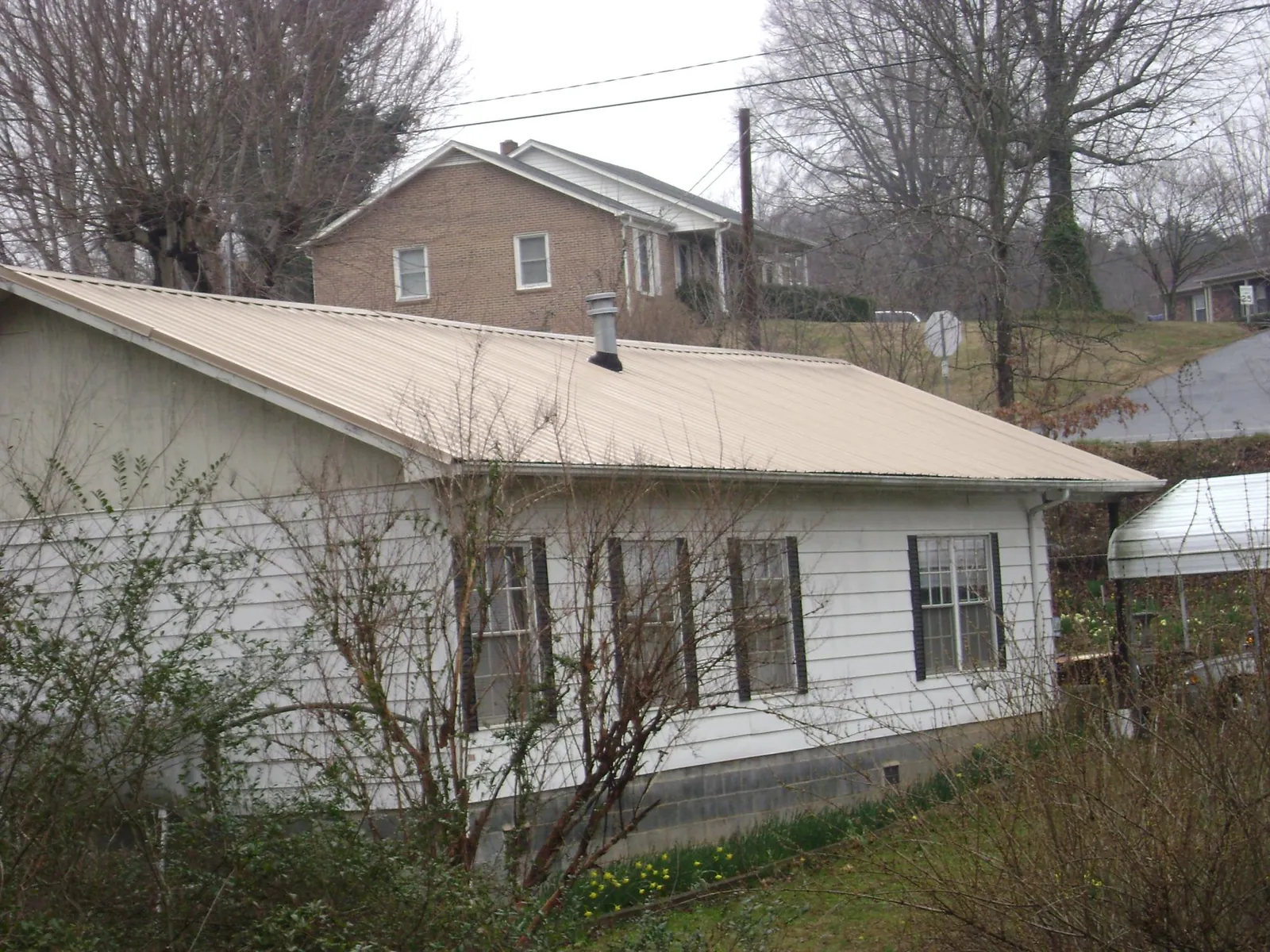 Tan metal roof on a white sided house set into a hillside — Commercial Roofing by Roofing Brothers in Morven