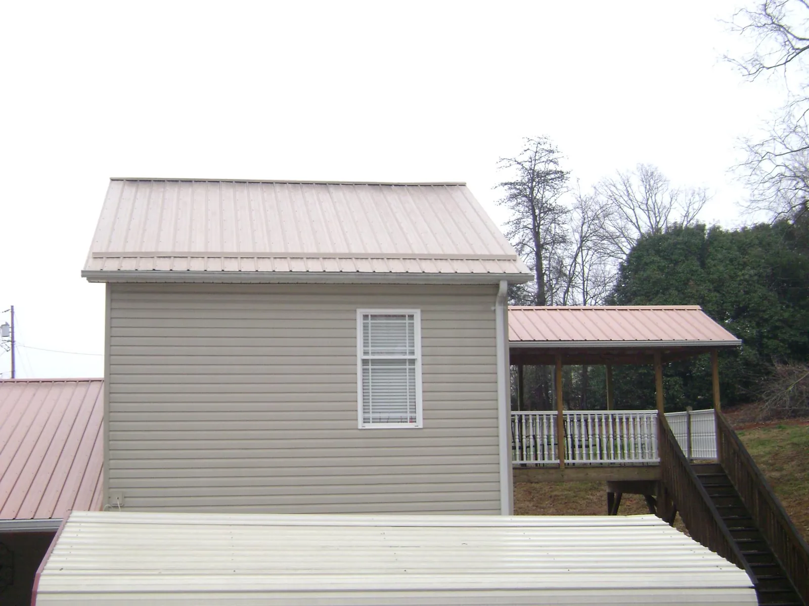 Tan metal roofs on a two story addition and attached porch, from a Roof Replacement job in Morven